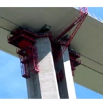Image d'un chantier de construction où un ouvrier verse un adjuvant liquide dans une bétonnière, avec un bâtiment en arrière-plan.